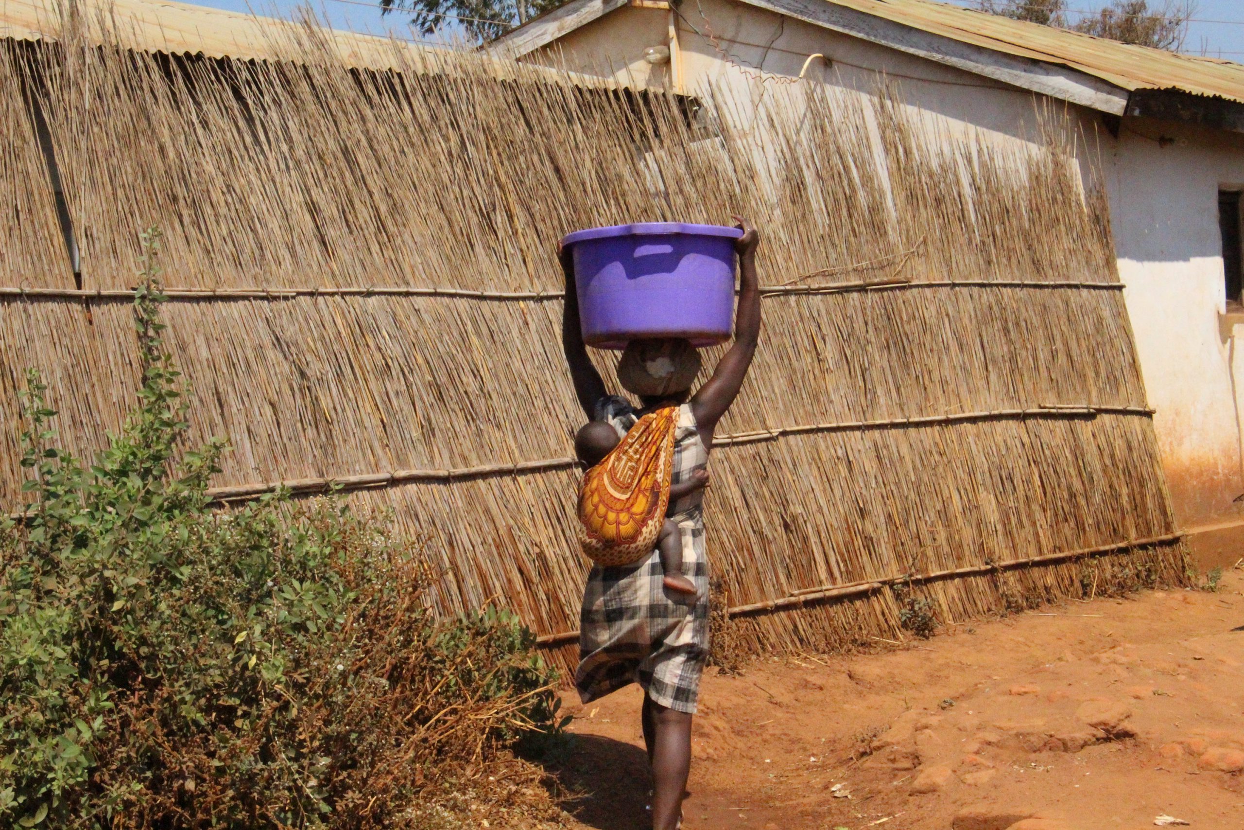 A woman in Malawi carries a 30-liter container of water on her head while also carrying an infant who is strapped to her back. Photo from Ellis Adjei Adams.